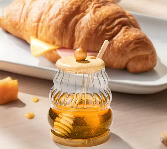 Glass honey storage jar with wooden lid and stirring stick